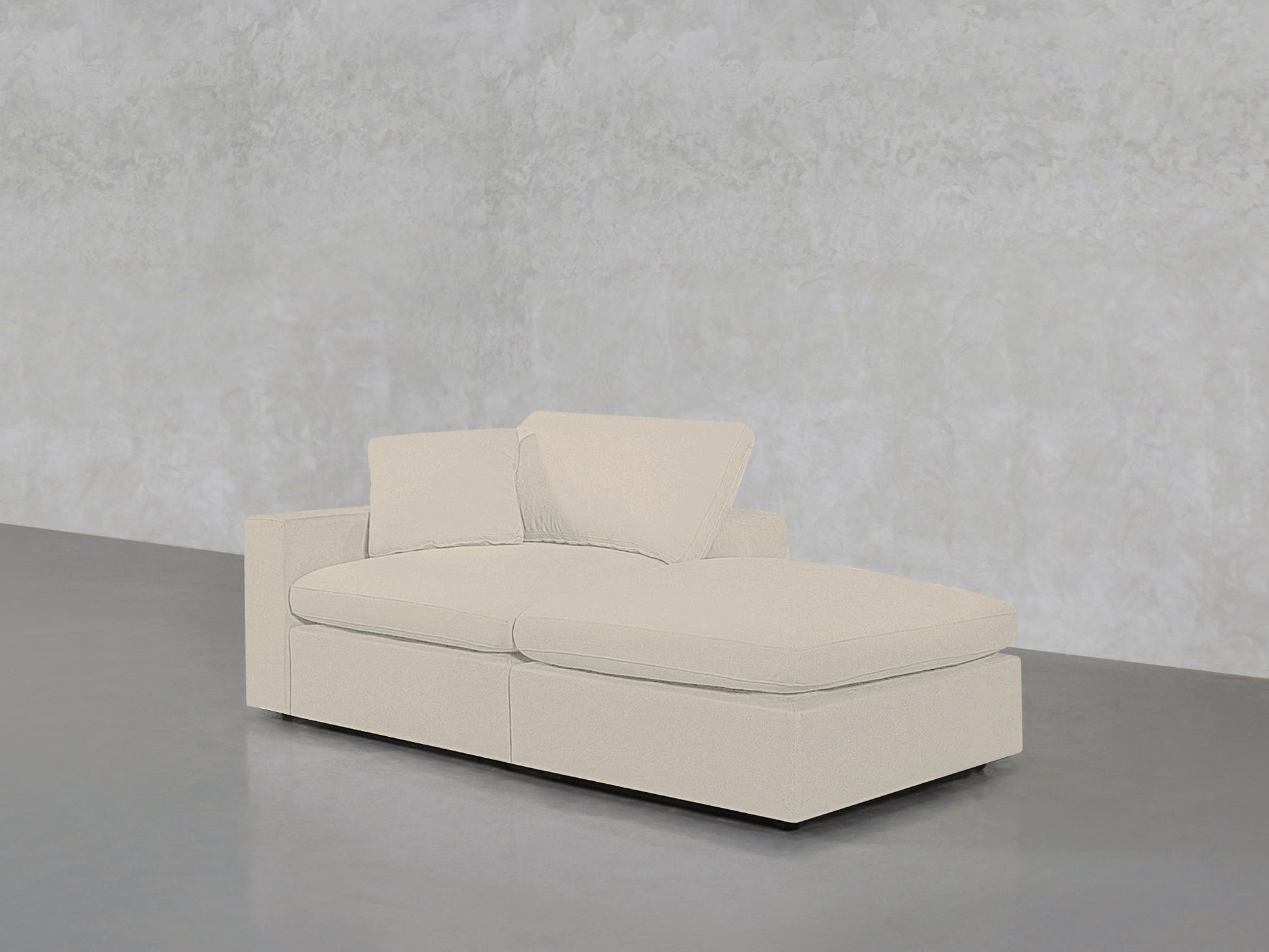 The 2-Seat Modular Lounger Loveseat in light beige, featuring two back cushions, is placed on a smooth gray floor against a textured light gray wall.