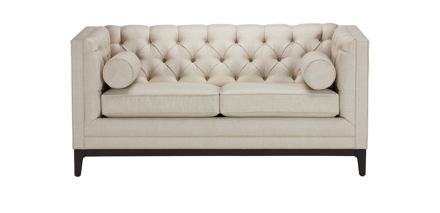 The Anderson Loveseat features a beige tufted design with two seat cushions and two bolster pillows. It has a high back and sides, supported by dark wooden legs.