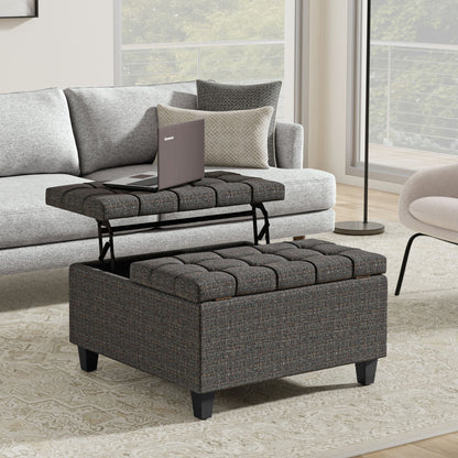 The Harrison Upholstered Coffee Table Storage Ottoman with a lift-top tray holding a laptop sits in front of a light gray sofa and next to a beige armchair in a modern living room with large windows.