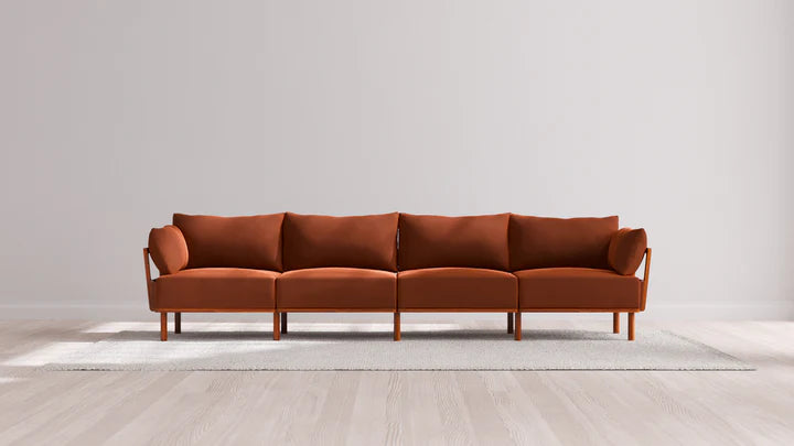 The Indoor Jack 4-Seater Sofa in Balsa, featuring a modern design and four cushions, is placed against a light gray wall. It sits atop a light-colored area rug on a wooden floor, creating a minimalist and elegant living space.