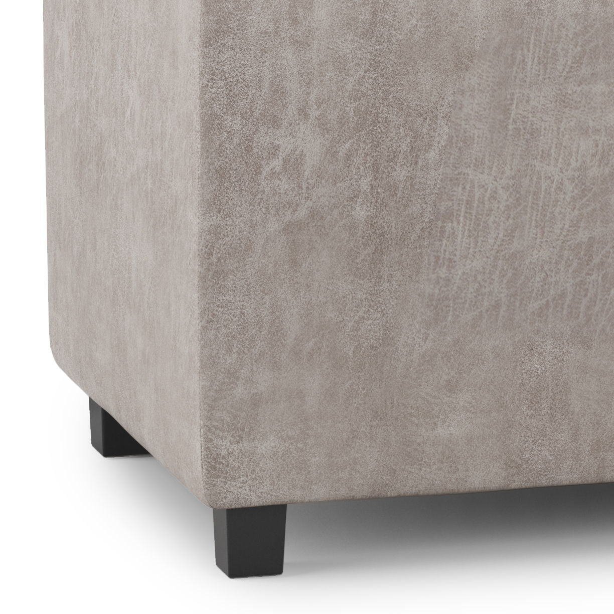 Close-up of the bottom corner of the Avalon - Upholstered Storage Ottoman in light beige fabric, featuring short black legs, shown on a white background.