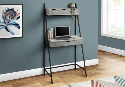 The Computer Desk For Home Office features black metal legs, gray shelves, three storage drawers, and an upper shelf with a potted plant. An open laptop sits on the desk against a blue wall near a framed flower print. Contemporary & modern style.