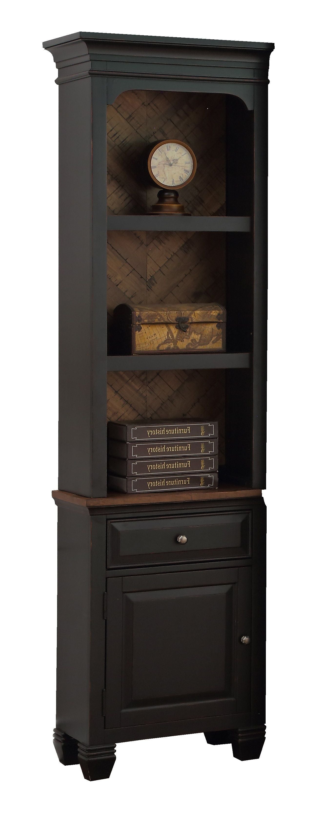 The Brighton - Pier is a tall, narrow black bookshelf with three shelves: a round clock on top, a decorative chest in the middle, books on the bottom shelf, and a lower cabinet with a silver knob.