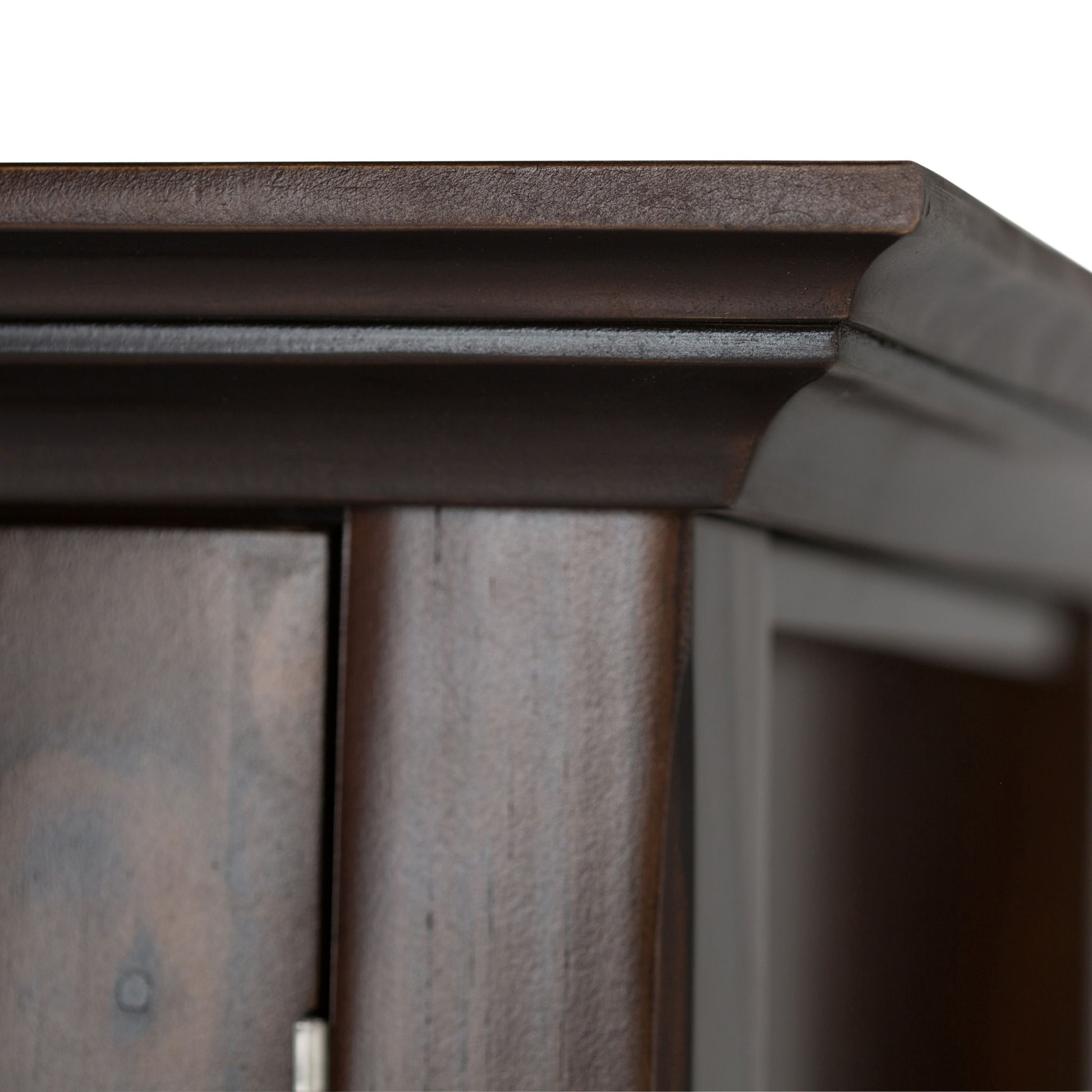 Close-up of the top corner of the Acadian Low Storage Cabinet in Brunette Brown, highlighting its detailed molding and smooth, polished dark wood finish against a white background.