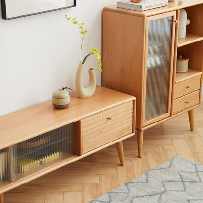 A TV Cabinet with Chinese Changhong glass doors and two drawer storage stands on a light herringbone floor. On top, there's a modern vase with yellow flowers and a small ceramic jar. A blue patterned rug is partially visible.