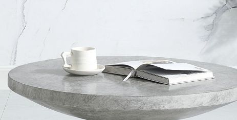 The Laddie - Weathered Table, round and gray, displays an open book and a white cup on a saucer against a light marble wall background.