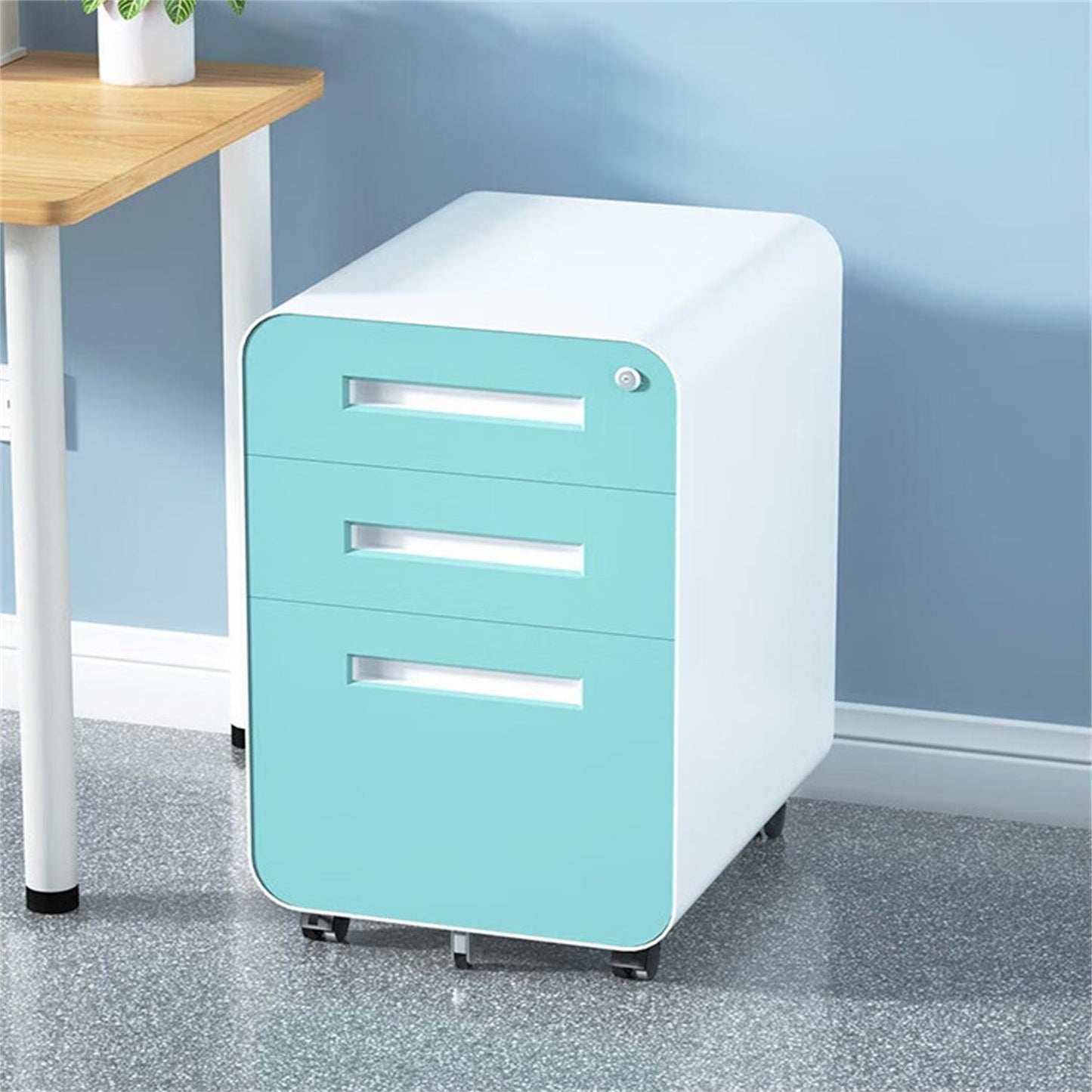 A 3 Drawer Mobile File Cabinet with a sleek white frame and turquoise drawers, featuring a 5-wheel anti-tilt design and waterproof steel, sits beside a desk against a light blue wall on a speckled gray floor.
