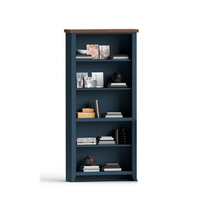 The Couch.com Nantucket 5 Shelf Bookcase in Blue Denim and Whiskey wood finish stands against a white background, its shelves arranged with books, papers, photo frames, decor items, and a ceramic vase.
