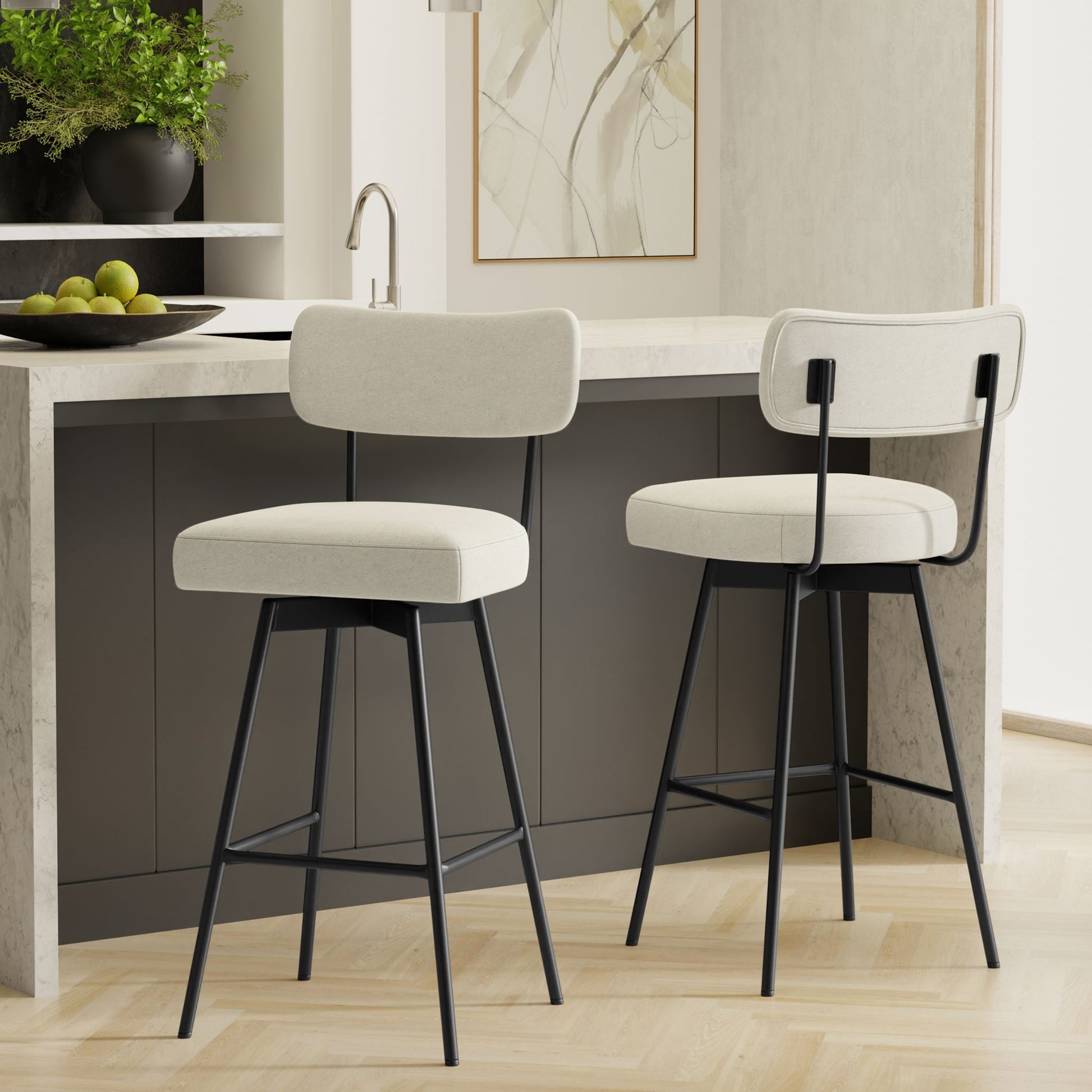 The Giselle Swivel Counter Height Stools (Set of 2) with cream upholstery and black metal frames are placed at a gray kitchen island with a marble countertop in a contemporary kitchen setting.