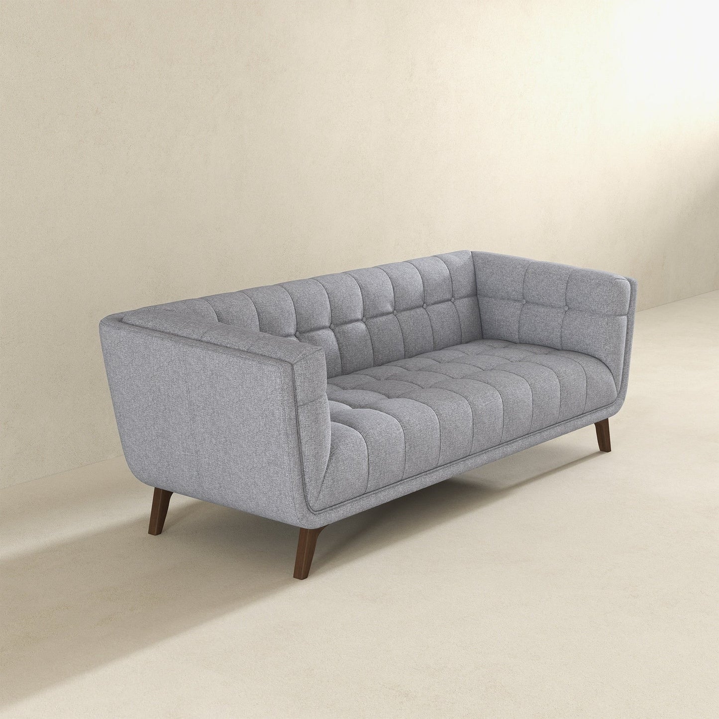 The Addison Mid-Century Modern Design Tufted Sofa, upholstered in gray with wooden legs, sits on a light beige floor against a plain, light-colored wall.