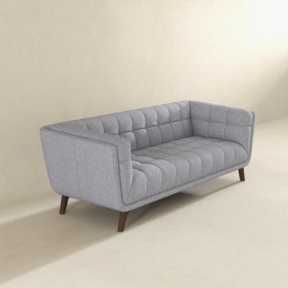 The Addison Mid-Century Modern Design Tufted Sofa, upholstered in gray with wooden legs, sits on a light beige floor against a plain, light-colored wall.