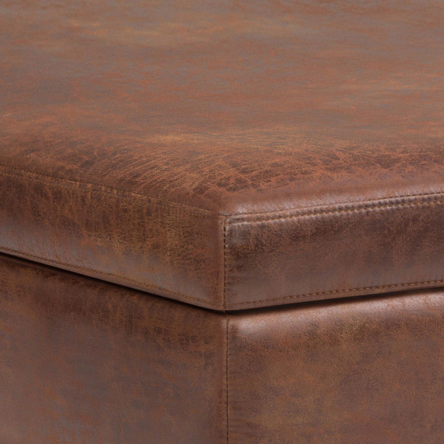 A close-up of the Owen - Multifunctional Square Coffee Table Storage Ottoman highlights its brown leather finish, textured and distressed details, and fine stitching on the corner.