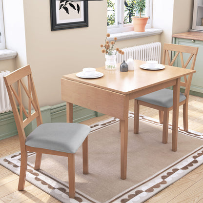 A 3 Piece Kitchen Dining Set with a drop leaf table and 2 upholstered chairs is placed on a beige rug in a bright kitchen with light green cabinets, set with white plates and cups near a window—perfect for small spaces.