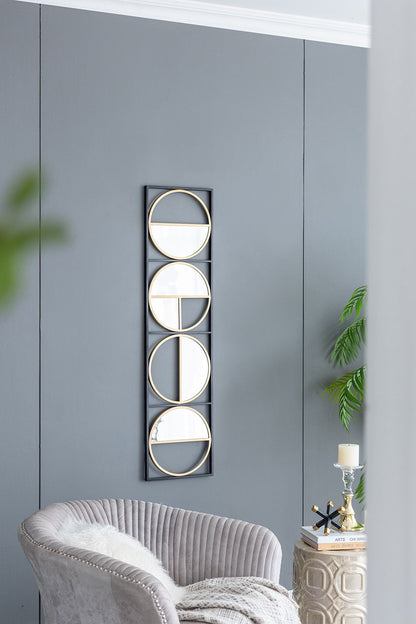 A modern living room with gray walls showcases the Eclectic Styling Metal Beaded Wall Mirror, featuring four gold-framed circular mirrors. Nearby are a plush gray chair, a small candlelit table, and a leafy plant for decoration.