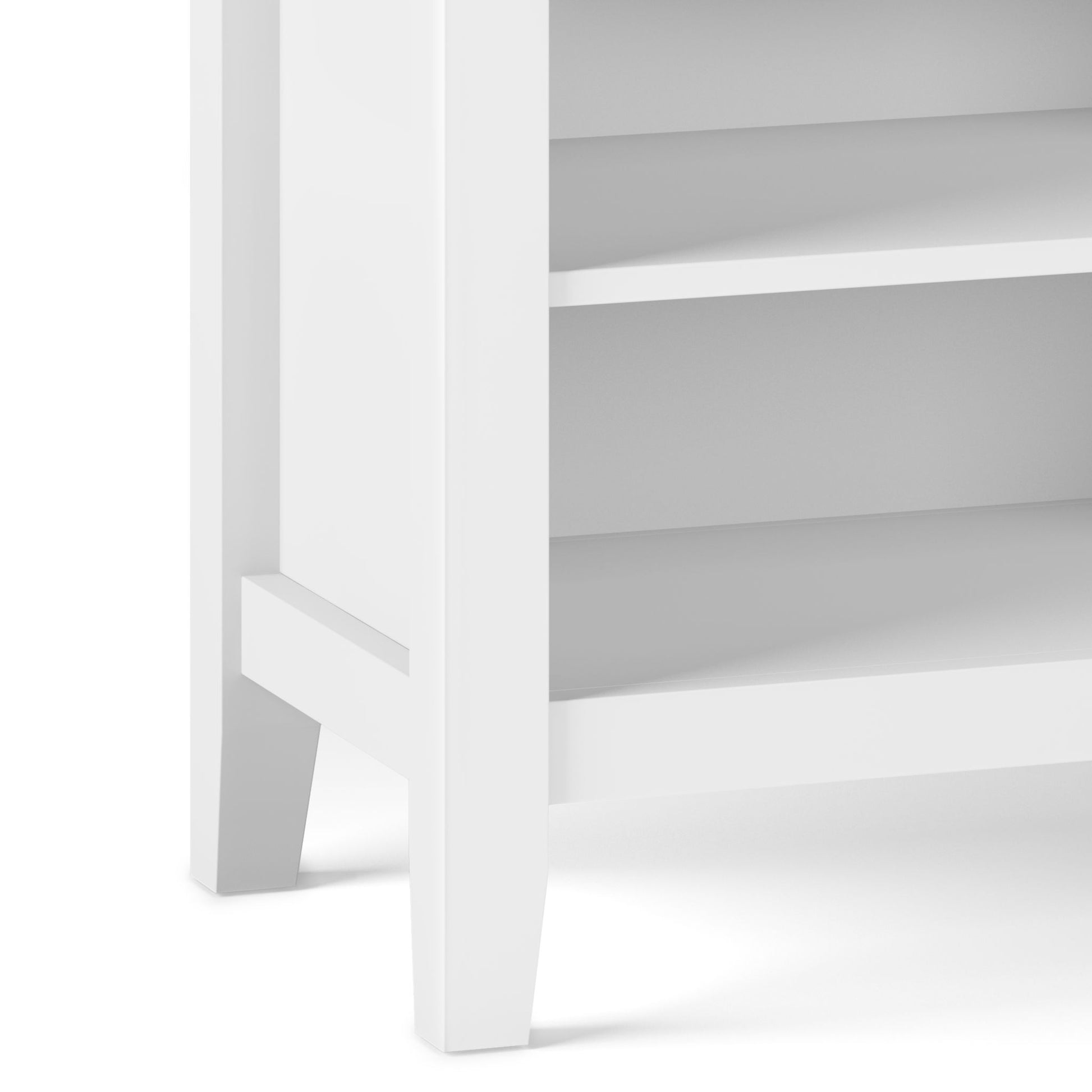 Close-up of the bottom corner of the Artisan - Handcrafted Bedside Table, highlighting two shelves and sturdy legs. The white wooden construction showcases a simple, modern design.