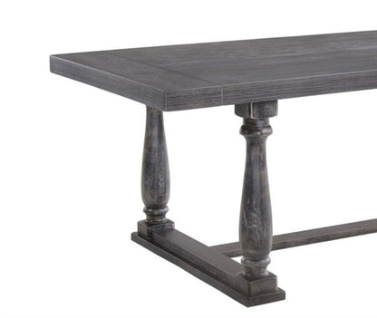 The Bernard - Weathered Dining Table features a dark wooden rectangular top and two turned pedestal legs connected by a horizontal base.