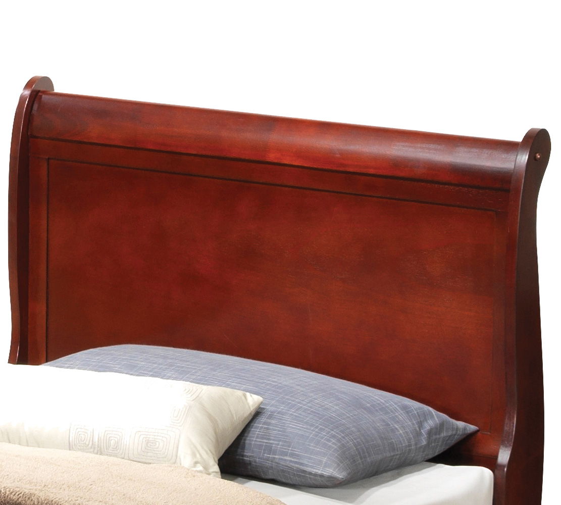 A close-up of the Panel Sleigh Bed’s dark wooden, curved headboard, shown behind a bed featuring a blue-gray pillow, a patterned accent pillow, and a beige blanket.