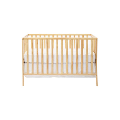 The Palmer - 3-in-1 Convertible Island Crib features vertical slats and a light wood finish, shown from the front with a white mattress and bedding against a plain white background.