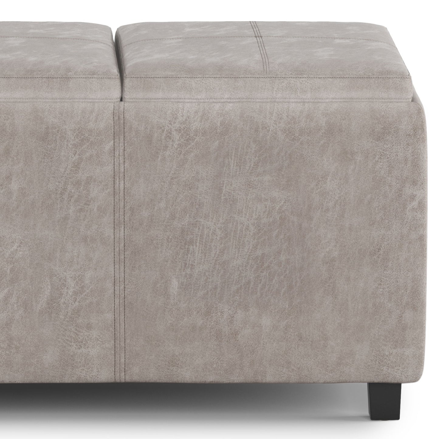 A close-up of the Avalon - Upholstered Storage Ottoman in light gray, featuring visible stitching, black legs, and a textured leather-like upholstery.