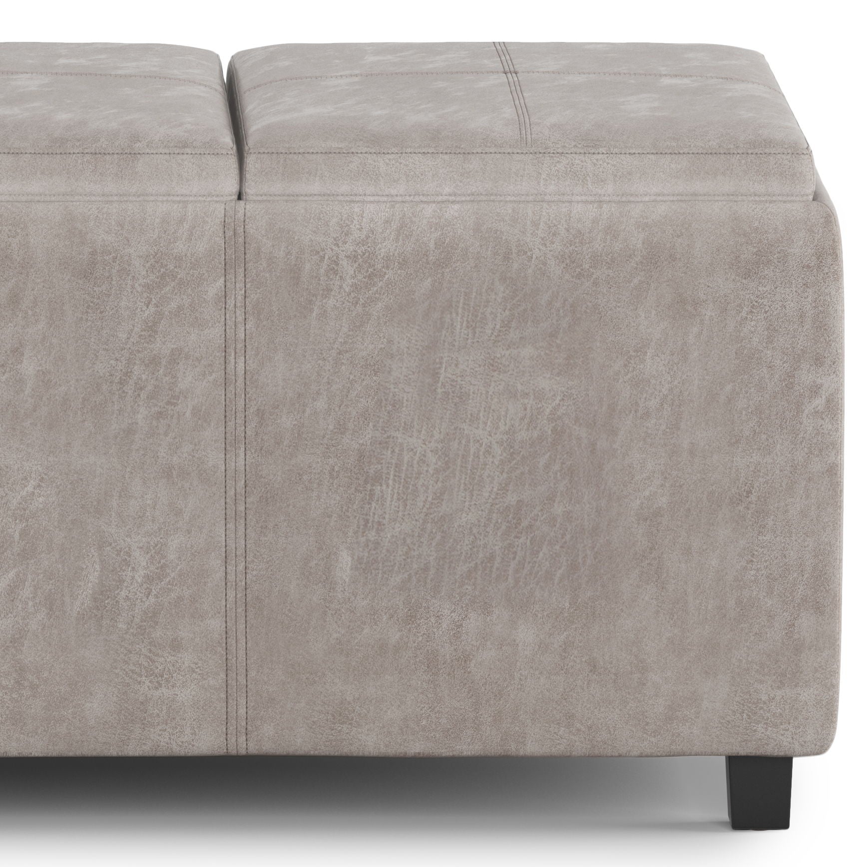 A close-up of the Avalon - Upholstered Storage Ottoman in light gray, featuring visible stitching, black legs, and a textured leather-like upholstery.