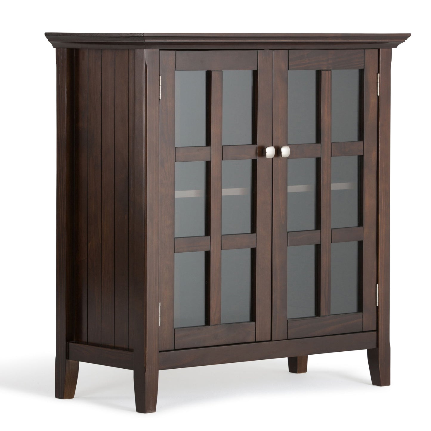 The Acadian Low Storage Cabinet in Brunette Brown features two glass-paneled doors with a grid pattern, silver knobs, square legs, and a modern design. An interior shelf is visible through the doors.