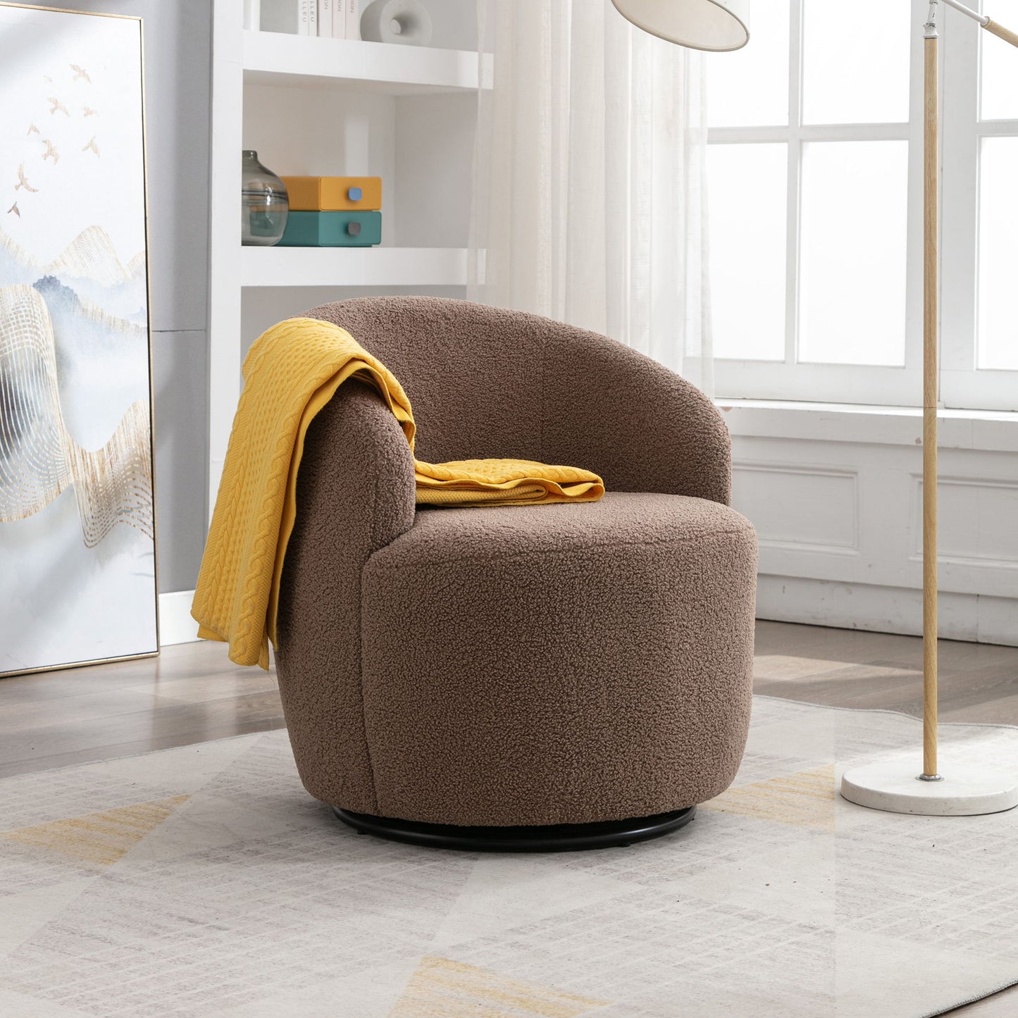 A Teddy Fabric Swivel Accent Armchair Barrel Chair with a powder coating metal ring sits on a patterned rug by a large window, draped with a yellow blanket. A floor lamp and shelves with books are in the background.