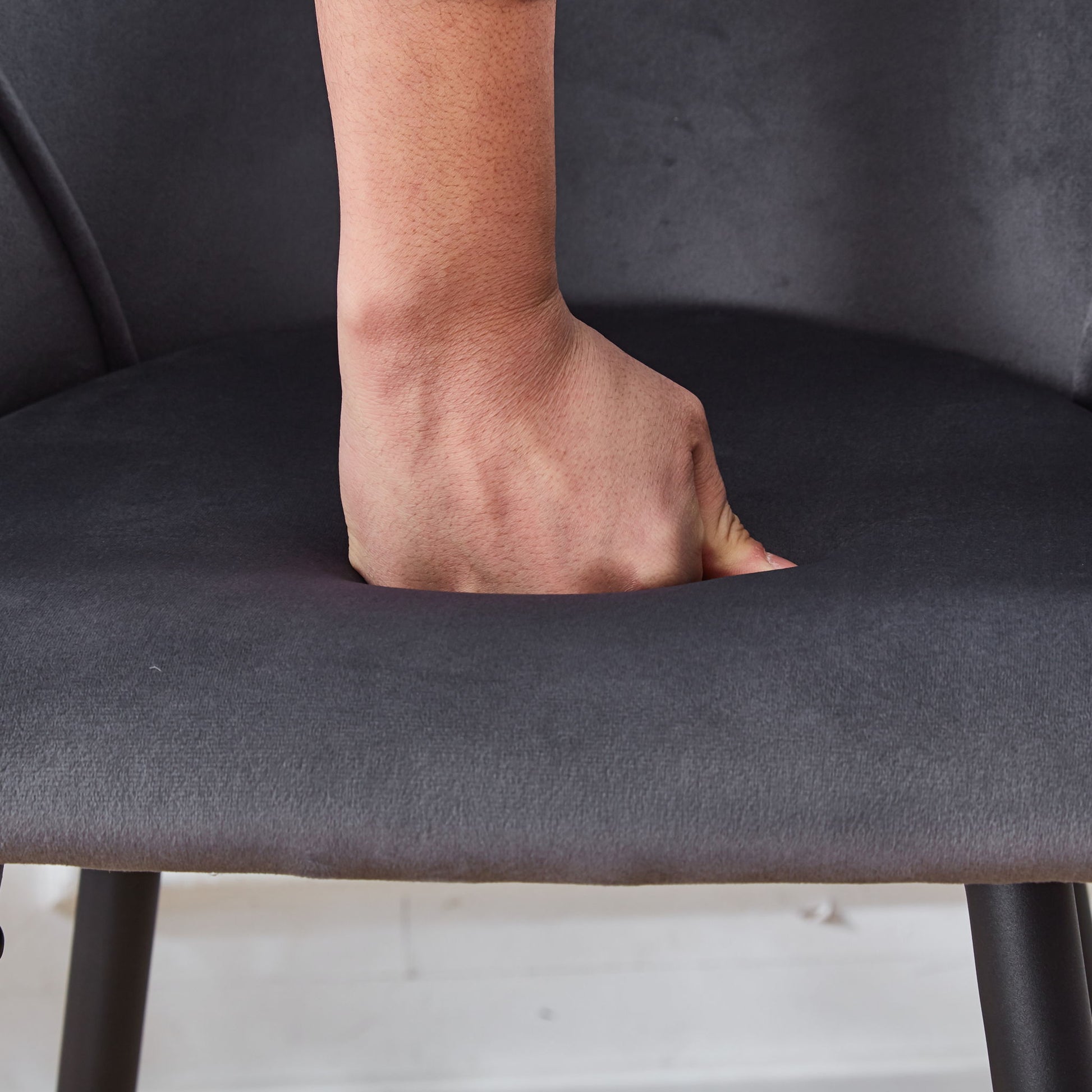A hand presses down on the cushioned seat of the Counter Height Bar Stool Metal Legs (Set of 2) in dark gray, highlighting the softness and indentation of the fabric.