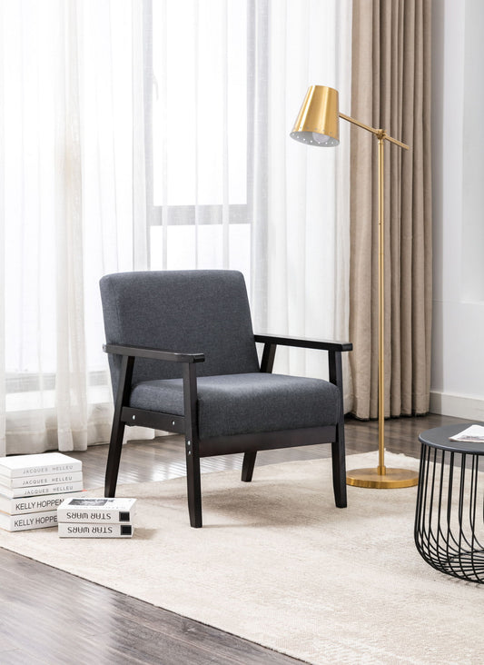 A modern living room features the Bahamas - Linen Fabric Chair in gray, a gold floor lamp, a round black side table with stacked books on a beige rug, and large windows dressed in sheer curtains and beige drapes that let in natural light.