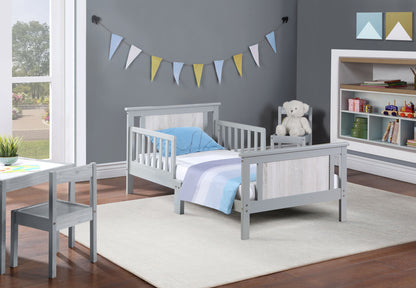A cozy kids’ bedroom features the Connelly Reversible Panel Toddler Bed in gray, striped bedding, a matching chair, shelves with books and toys, a teddy bear on the nightstand, pennant banners on a gray wall, and a white rug.