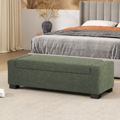 A Textured Fabric Ottoman Bench With Hinged Lid in green sits at the foot of a bed with a gray headboard, beige carpet, and a decorative vase with yellow branches in a modern bedroom.