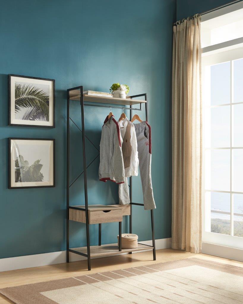 The Metal Clothes Rack Open Wardrobe with a drawer and hanging rod stands against a teal wall, organizing clothes, a basket, and decor. Two framed prints hang nearby as sunlight fills the space from a large window with beige curtains.