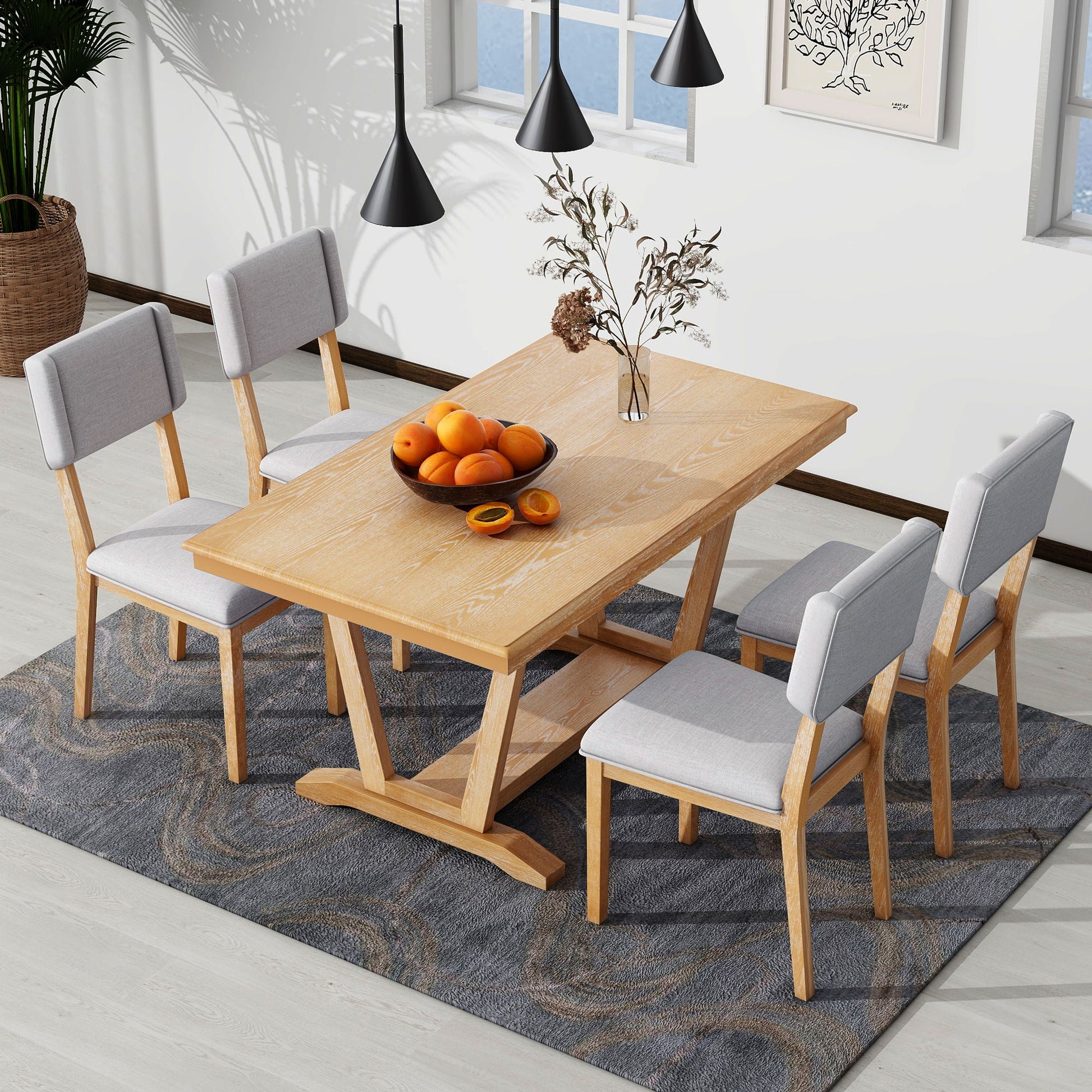 The Topmax 5 Piece Rustic Dining Table Set features a rectangular trestle-base table and 4 upholstered chairs, arranged on a patterned rug with a bowl of oranges and dried flowers, in a bright room with large windows.
