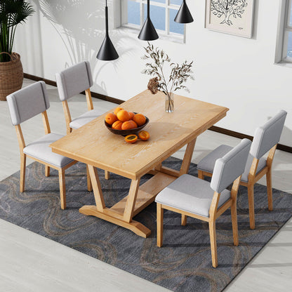 The Topmax 5 Piece Rustic Dining Table Set features a rectangular trestle-base table and 4 upholstered chairs, arranged on a patterned rug with a bowl of oranges and dried flowers, in a bright room with large windows.