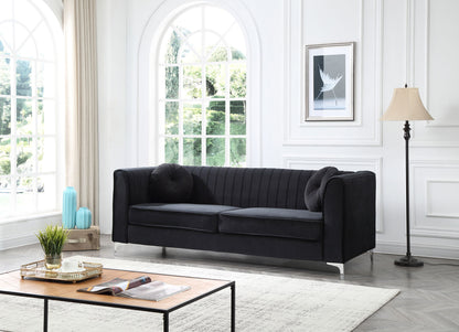A modern living room with the Delray - Micro Suede Sofa in black, two matching cushions, a wooden coffee table with books and a plant, light walls, large arched windows, framed art, blue vases, and a floor lamp.