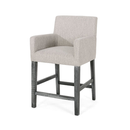 The Charmed Upholstered Counter Stool features round arms, a light gray upholstered seat, back and arms, plus four dark wooden legs with an H-frame base for support.