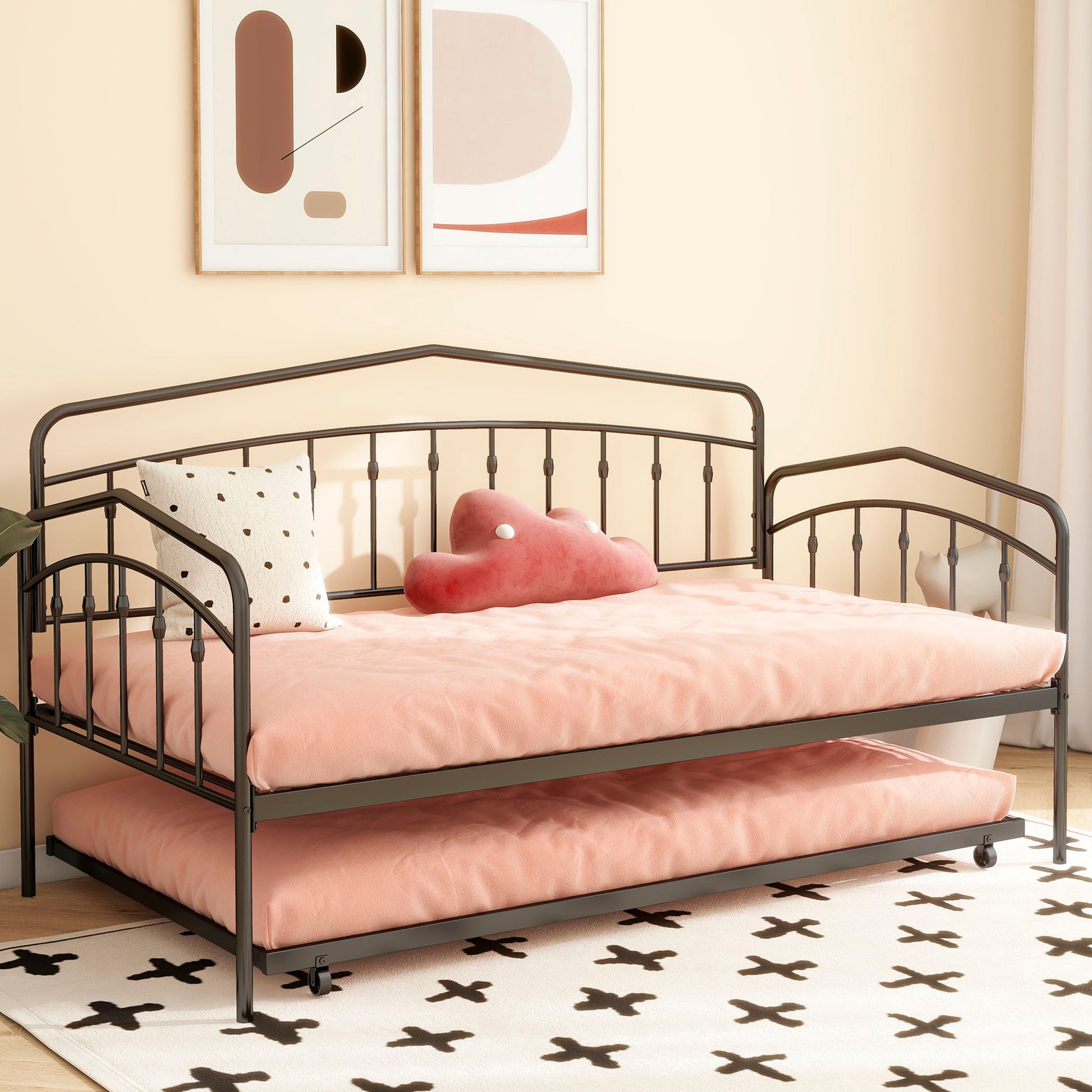 The Fox - Daybed With Twin Trundle in black metal, topped with pink bedding and decorative pillows, is set against a light peach wall under abstract art. A white rug with black X patterns lies on the floor.