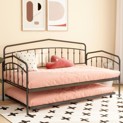 The Fox - Daybed With Twin Trundle in black metal, topped with pink bedding and decorative pillows, is set against a light peach wall under abstract art. A white rug with black X patterns lies on the floor.