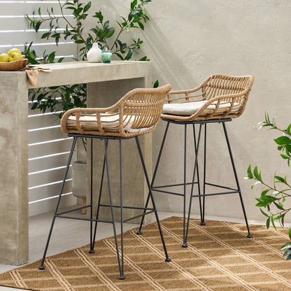 Two Outdoor Rattan Bar Chairs With Metal Legs and cushions are placed by a concrete counter in a bright, modern patio with green plants and a woven rug on the floor.