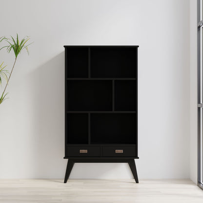 The Draper - Mid Century Wide Bookcase And Storage Unit, featuring open shelves and two bottom drawers in black, stands against a white wall near a window. A green potted plant is to the left on the light wooden floor.