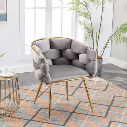 A Luxury Modern Simple Leisure Velvet Single Sofa Chair with gold legs sits on a rug beside a small round table and potted plant in a bright room with large windows.