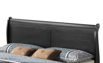 The Panel Sleigh Bed features a dark wood headboard with a simple, modern design, displayed behind a neatly made bed dressed in patterned blue and gray bedding and accented with brown pillows.