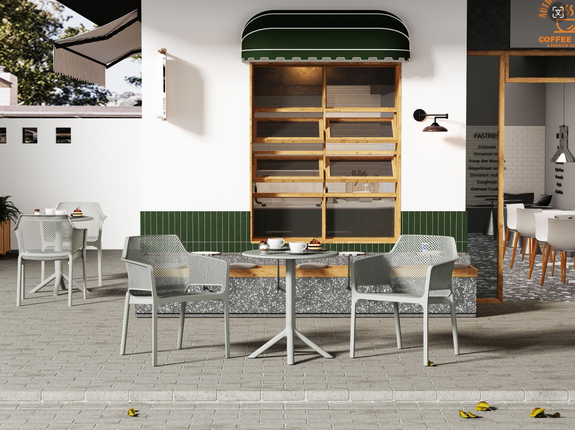 Outdoor café seating area featuring 3 Piece Plastic Arm Chair Bistro Grs Premium Ocean Plastic sets on a stone patio, with modern gray chairs and tables, in front of a building with a green awning and empty wooden shelves. Pastries and drinks adorn the tables.