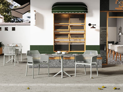 Outdoor café seating area featuring 3 Piece Plastic Arm Chair Bistro Grs Premium Ocean Plastic sets on a stone patio, with modern gray chairs and tables, in front of a building with a green awning and empty wooden shelves. Pastries and drinks adorn the tables.