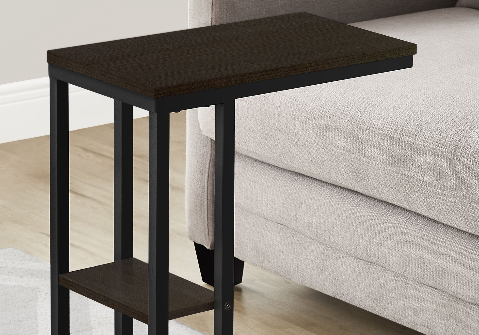 The Accent Table C-Shaped, Contemporary & Modern features dark wood and black metal, a rectangular top, lower shelf, and sits beside a light gray couch on a light wood floor.
