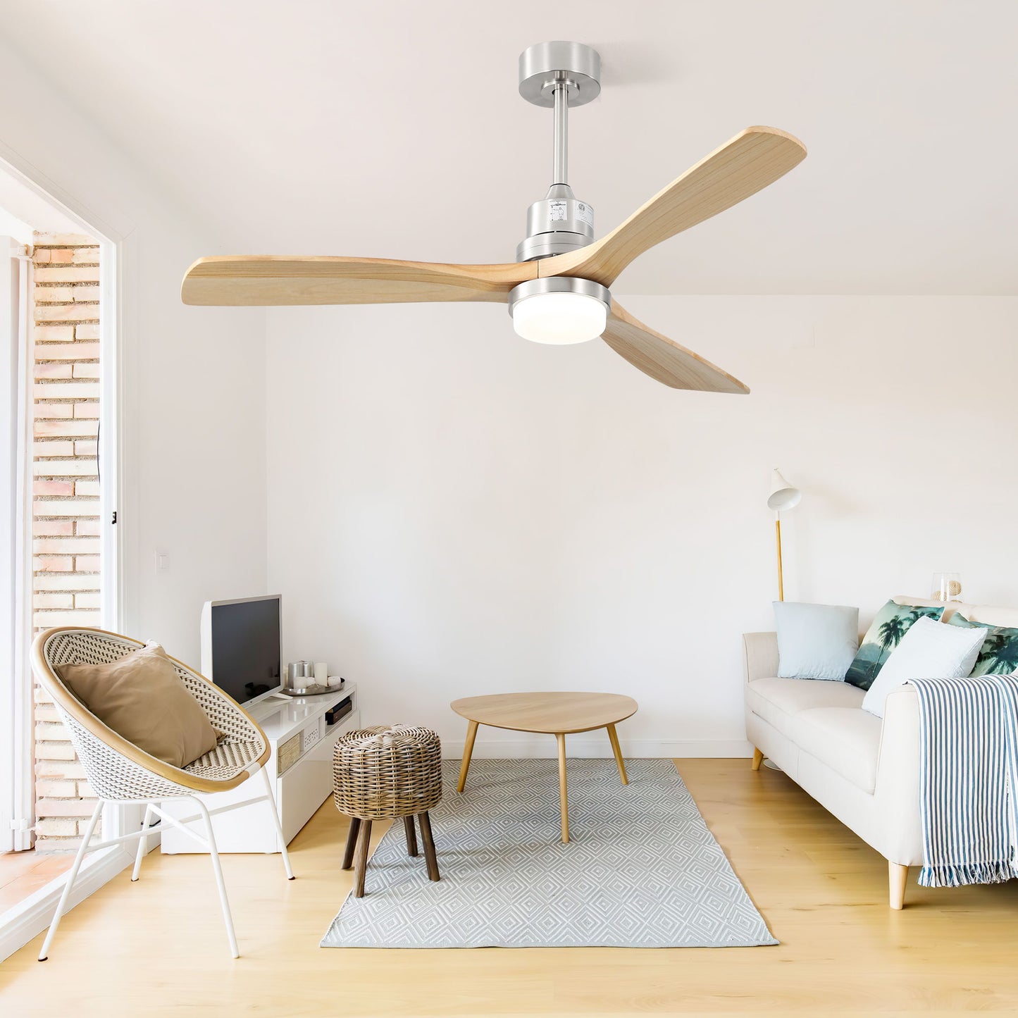 Modern living room with light wood flooring, a white sofa with green and blue pillows, a round coffee table, wicker stools, TV, and a Ceiling Fan With Dimmable LED Light 6 Speed Remote 3 Wood Blade Reversible DC Motor in brushed nickel.