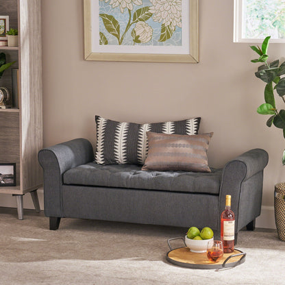 A modern living room showcases the Hayes Contemporary Armed Storage Bench with rolled arms and button tufting, topped with two patterned pillows, a floral artwork above, and a tray holding a wine bottle, glass, and green apples in front.