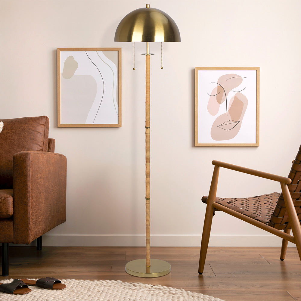 A modern living room corner with a brown leather sofa, woven chair, wood flooring, neutral decor, and the Allure 2 Light Floor Lamp in Gold with a Natural Tube and double pull chain beside two abstract prints on a cream wall.
