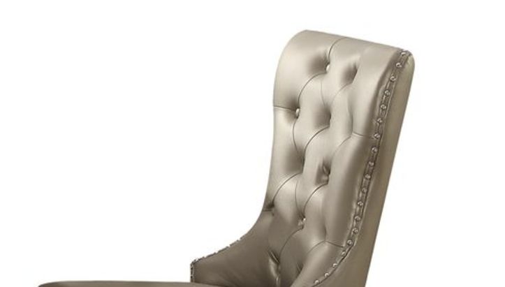The Kacela Synthetic Leather Side Chair (Set of 2) in Champagne features a high back, tufted design, shiny beige upholstery, and silver nailhead trim along the edges.