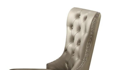 The Kacela Synthetic Leather Side Chair (Set of 2) in Champagne features a high back, tufted design, shiny beige upholstery, and silver nailhead trim along the edges.