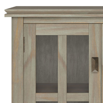 Close-up of the upper left corner of the Artisan - Handcrafted Low Storage Cabinet, showcasing its weathered gray finish, glass panel doors with vertical wooden frames, and a rectangular metal handle on the right door.